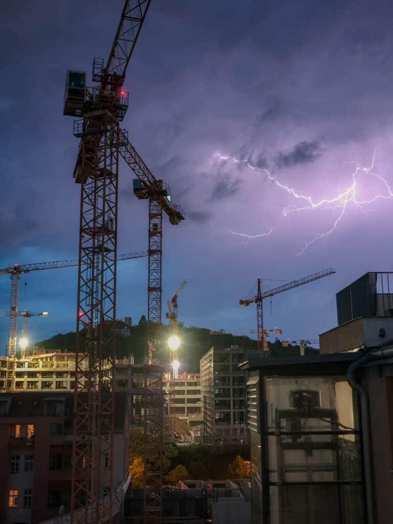 construction cranes against the night sky and lightning in a sto